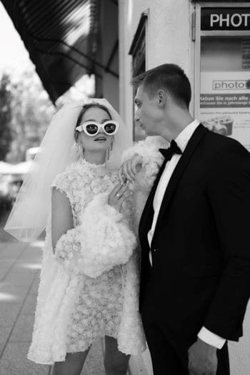 Moderne Braut mit kurzem Hochzeitskleid und Sonnenbrille, gemeinsam mit Bräutigam