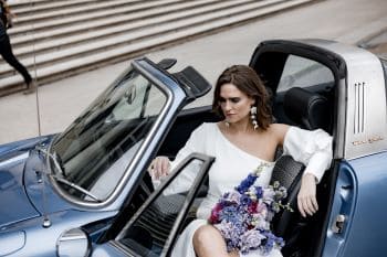 Braut in Hochzeitsauto mit lila Brautstrauß